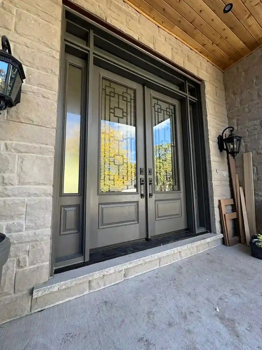 Grey fiberglass double entry doors with decorative patterned glass and a tall sidelight on a natural stone home